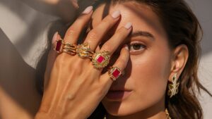 A person examining a gold ring with a magnifying glass at a countertop near natural light.